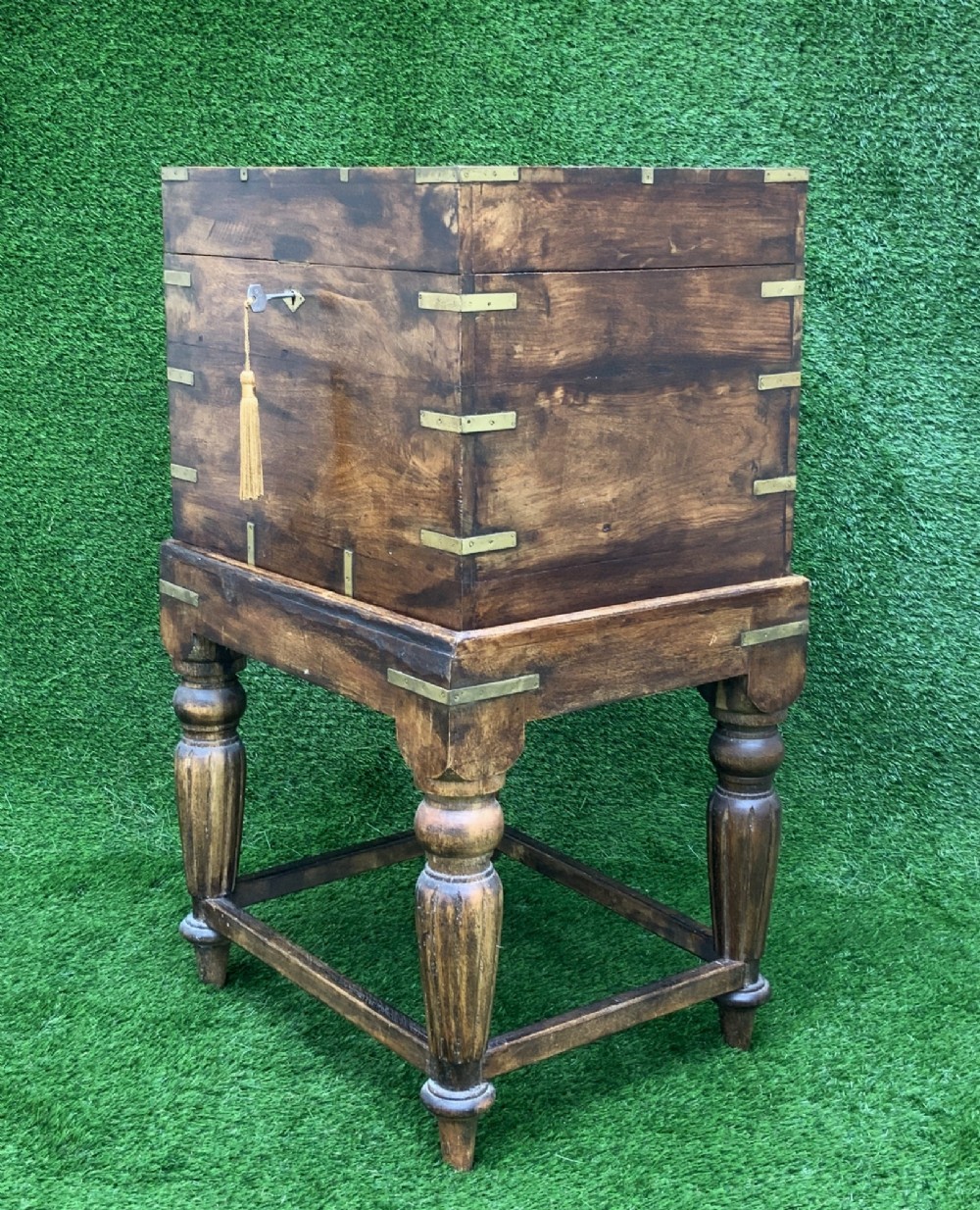 A dark teak Anglo-Indian wine cellarette box with brass corner mounts resting on a carved turned-leg wooden stand. View II