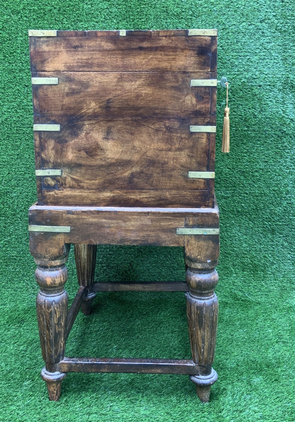 A dark teak Anglo-Indian wine cellarette box with brass corner mounts resting on a carved turned-leg wooden stand. View V