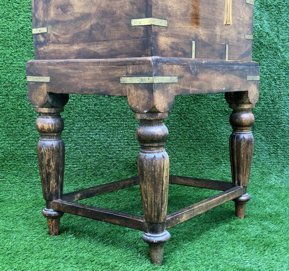 A dark teak Anglo-Indian wine cellarette box with brass corner mounts resting on a carved turned-leg wooden stand. View IX