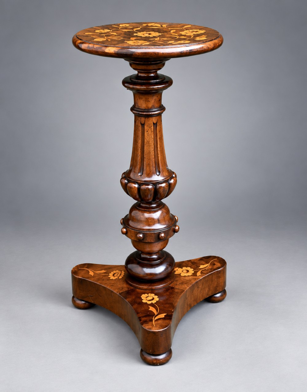 A 19th-century Dutch marquetry wine table featuring a circular floral-inlaid top, a carved central column, and a shaped triform base raised on bun feet.
