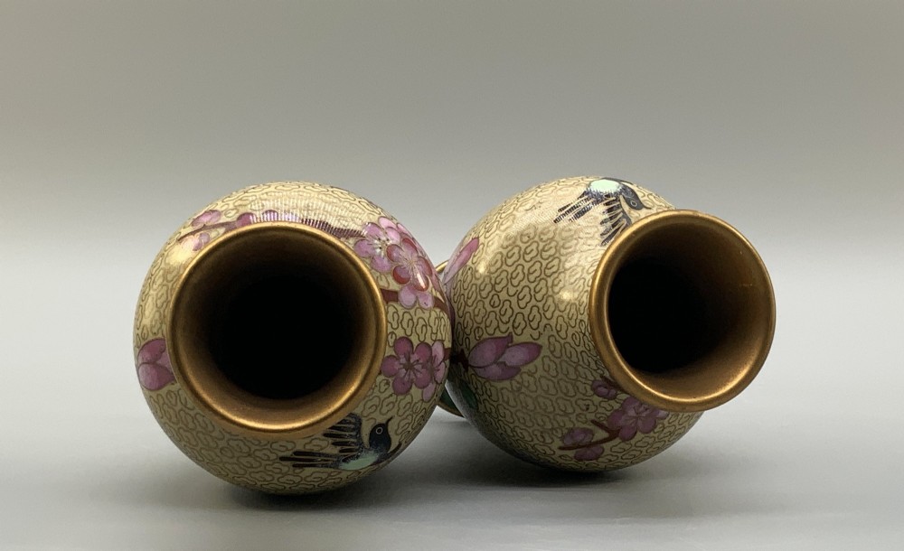 A pair of early 20th-century Chinese cloisonne enamel vases featuring pink prunus blossoms and bird motifs on a yellow cloud-scroll ground, resting on carved wooden stands. View II