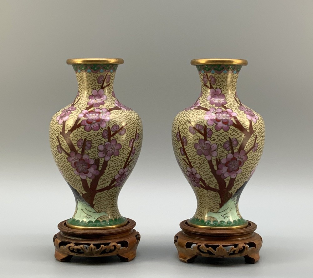 A pair of early 20th-century Chinese cloisonne enamel vases featuring pink prunus blossoms and bird motifs on a yellow cloud-scroll ground, resting on carved wooden stands. View III