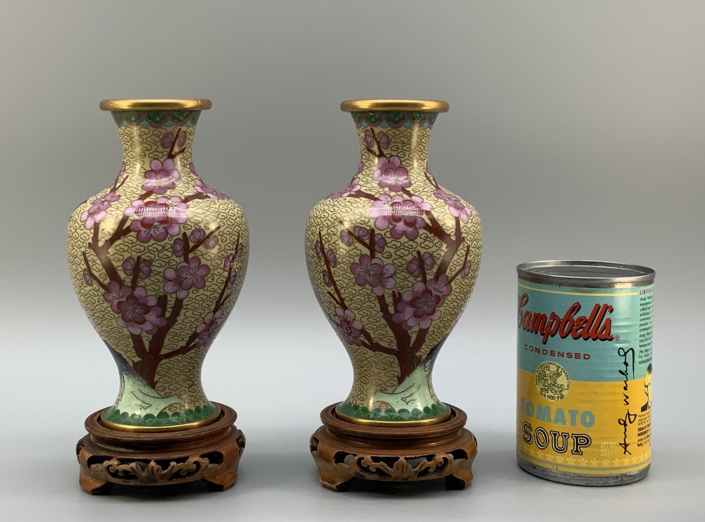 A pair of early 20th-century Chinese cloisonne enamel vases featuring pink prunus blossoms and bird motifs on a yellow cloud-scroll ground, resting on carved wooden stands. View IV