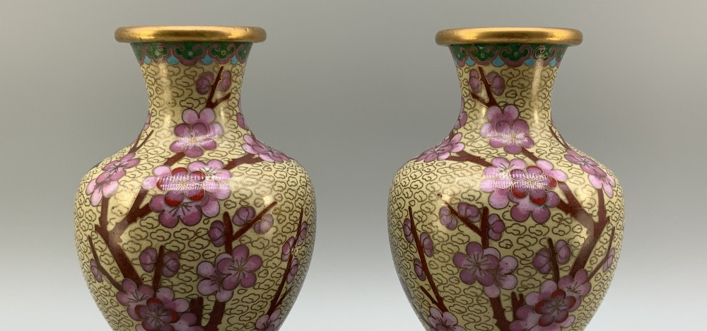 A pair of early 20th-century Chinese cloisonne enamel vases featuring pink prunus blossoms and bird motifs on a yellow cloud-scroll ground, resting on carved wooden stands. View V