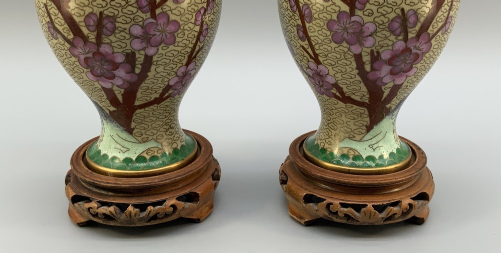 A pair of early 20th-century Chinese cloisonne enamel vases featuring pink prunus blossoms and bird motifs on a yellow cloud-scroll ground, resting on carved wooden stands. View VI