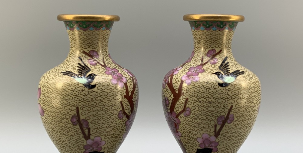 A pair of early 20th-century Chinese cloisonne enamel vases featuring pink prunus blossoms and bird motifs on a yellow cloud-scroll ground, resting on carved wooden stands. View VIII