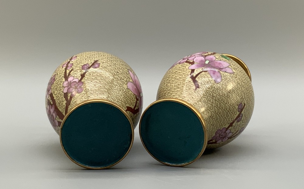 A pair of early 20th-century Chinese cloisonne enamel vases featuring pink prunus blossoms and bird motifs on a yellow cloud-scroll ground, resting on carved wooden stands. View XI