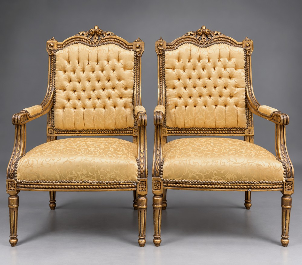 A pair of 19th-century giltwood open armchairs featuring carved leaf detailing, button-tufted gold damask upholstery, and fluted front legs.