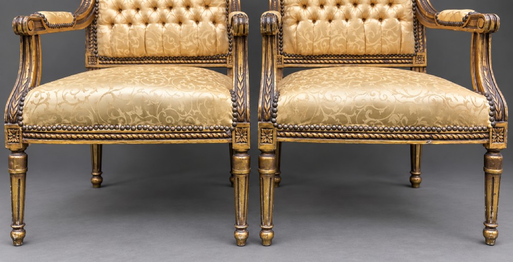 A pair of 19th-century giltwood open armchairs featuring carved leaf detailing, button-tufted gold damask upholstery, and fluted front legs. View IX