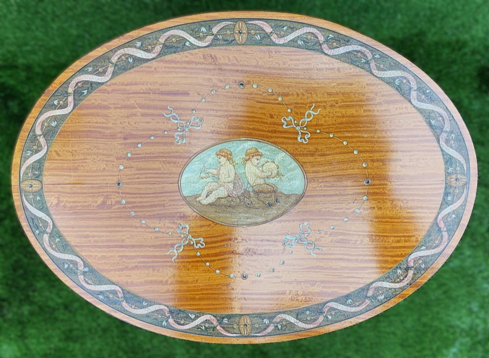 An oval satinwood sewing table featuring hand-painted floral swags, slender tapered legs, an X-form stretcher, and a pleated light blue fabric work basket suspended below. View VIII