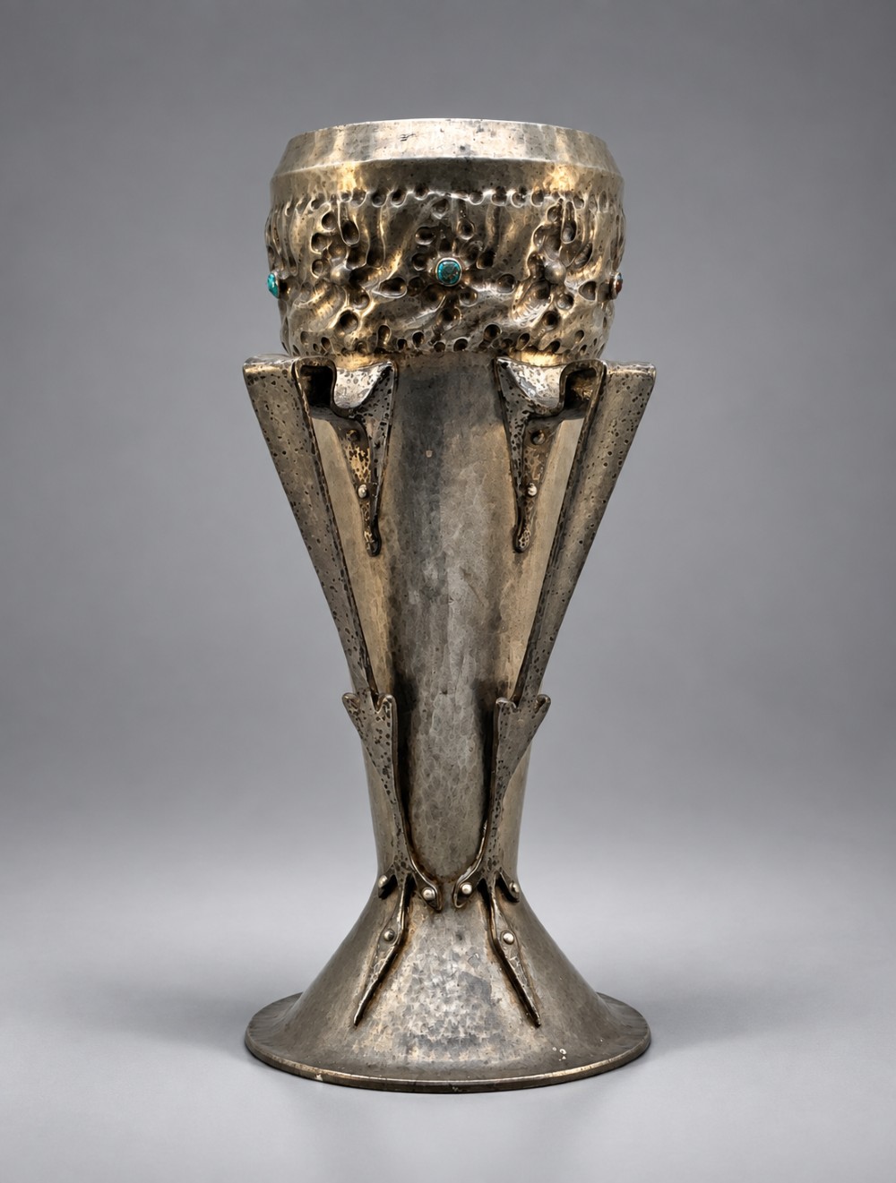 An Arts and Crafts hammered pewter vase featuring raised geometric support fins, a textured upper band, and inlaid turquoise cabochons.