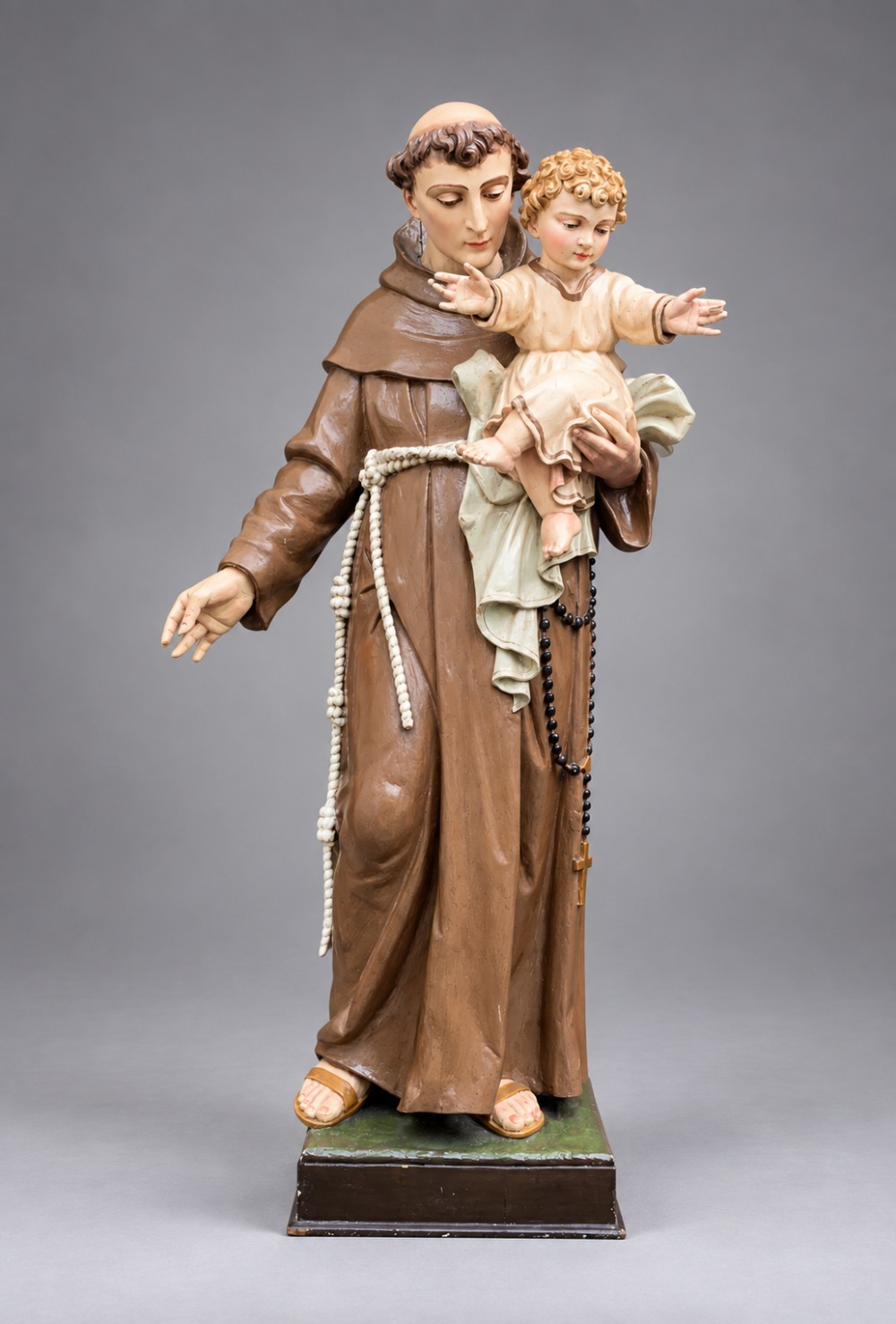 An antique polychrome carved wood sculpture depicting Saint Anthony in a brown Franciscan habit holding the Christ Child.