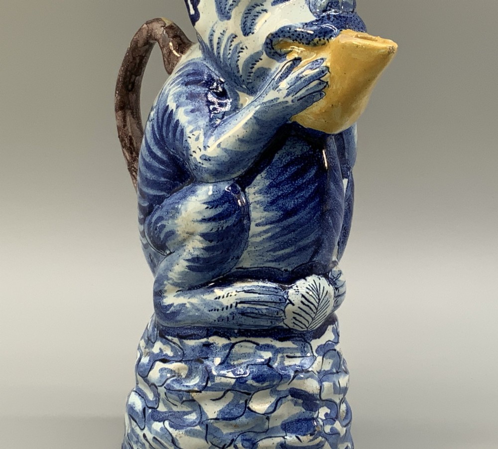 An 18th-century Dutch Delftware ceramic jug hand-painted in blue, white, brown, and yellow, designed in the form of a seated monkey in a tricorn hat holding a cup. View VII