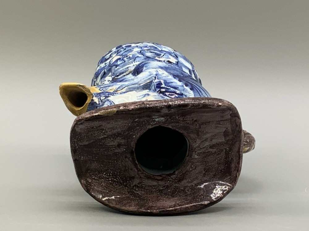 An 18th-century Dutch Delftware ceramic jug hand-painted in blue, white, brown, and yellow, designed in the form of a seated monkey in a tricorn hat holding a cup. View IX