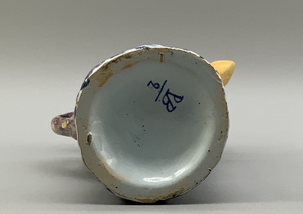 An 18th-century Dutch Delftware ceramic jug hand-painted in blue, white, brown, and yellow, designed in the form of a seated monkey in a tricorn hat holding a cup. View X