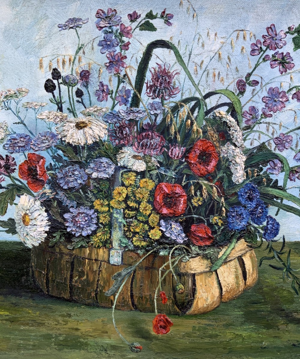 A framed floral still life oil painting depicting a woven basket filled with colourful wildflowers including poppies and daisies against a light blue backdrop. View VI