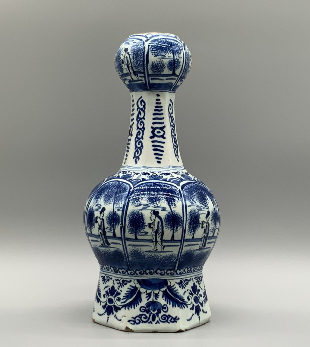A 17th-century hexagonal Dutch Delft blue and white faience vase decorated with hand-painted chinoiserie figures and floral motifs.