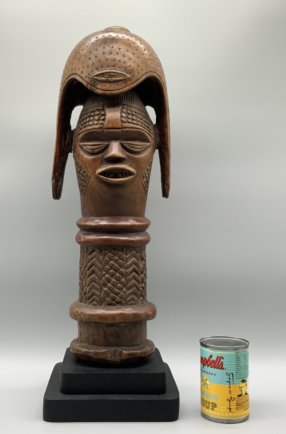 A carved brown wooden African Mende Sowei staff finial depicting a stylised head with crest, mounted on a square black plinth. View III