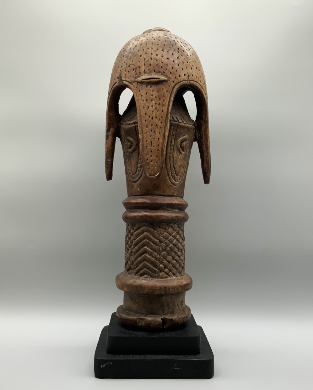 A carved brown wooden African Mende Sowei staff finial depicting a stylised head with crest, mounted on a square black plinth. View IV