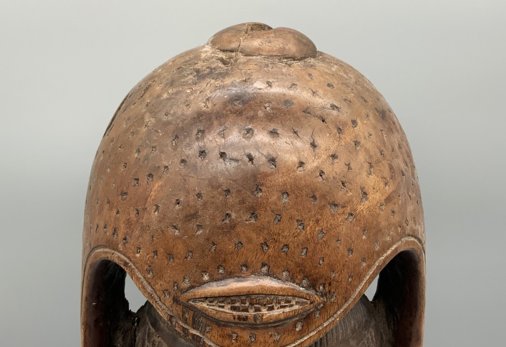 A carved brown wooden African Mende Sowei staff finial depicting a stylised head with crest, mounted on a square black plinth. View X
