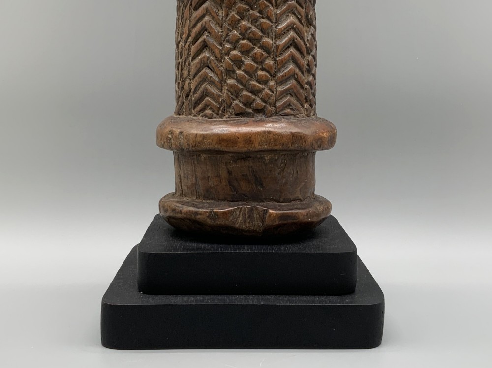 A carved brown wooden African Mende Sowei staff finial depicting a stylised head with crest, mounted on a square black plinth. View XI