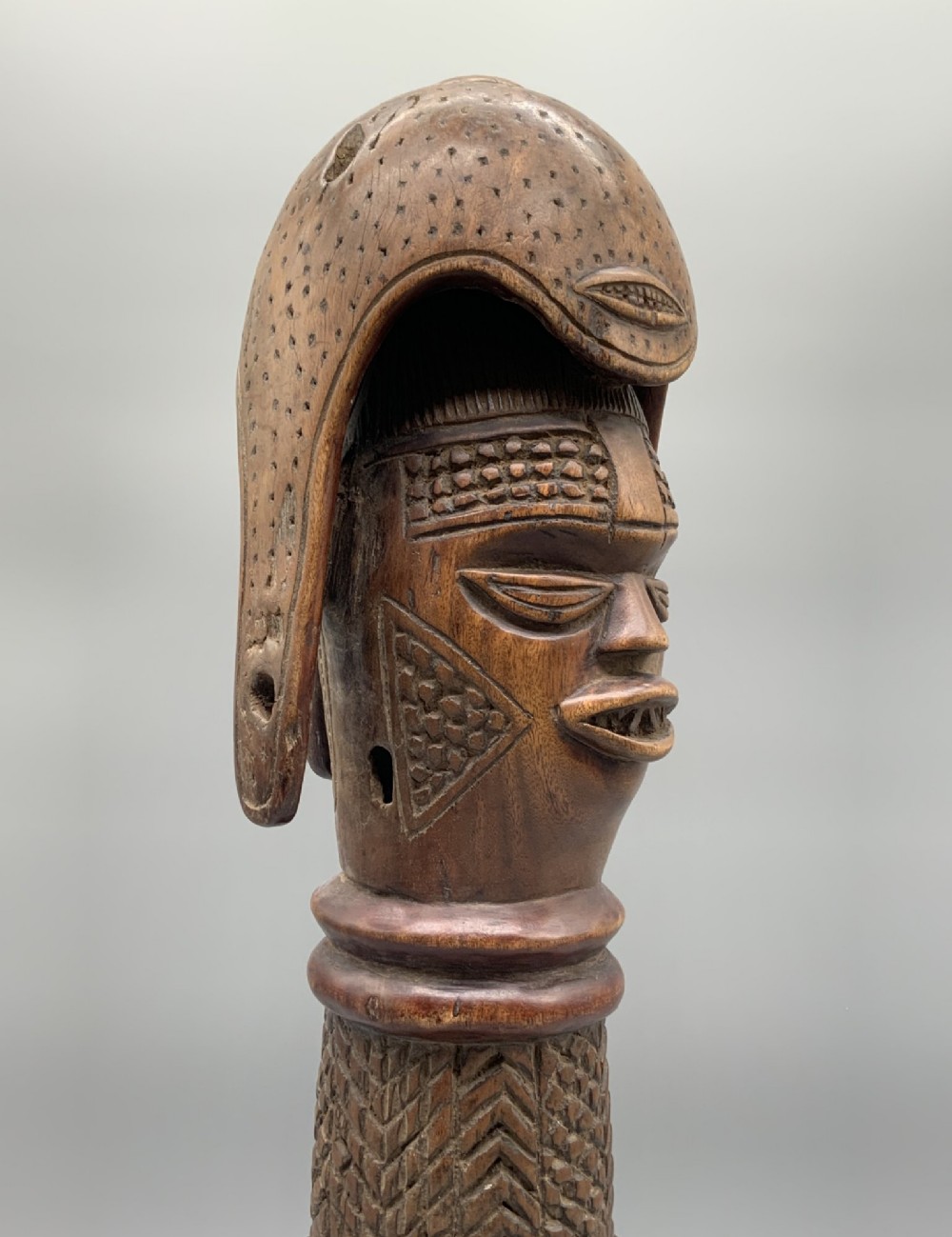 A carved brown wooden African Mende Sowei staff finial depicting a stylised head with crest, mounted on a square black plinth. View XII