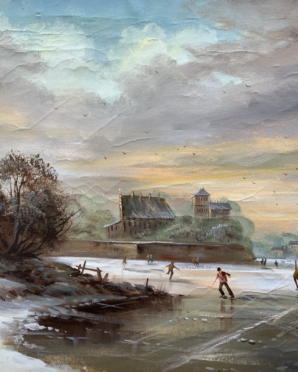 A large framed oil painting depicting figures ice skating on a frozen canal beside historic stone buildings under a winter sky, housed in an ornate gilt frame. View V