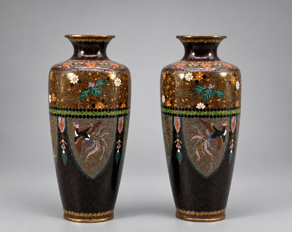A pair of Japanese Meiji period cloisonne enamel vases featuring detailed phoenix birds, floral motifs, and geometric borders on a dark background.