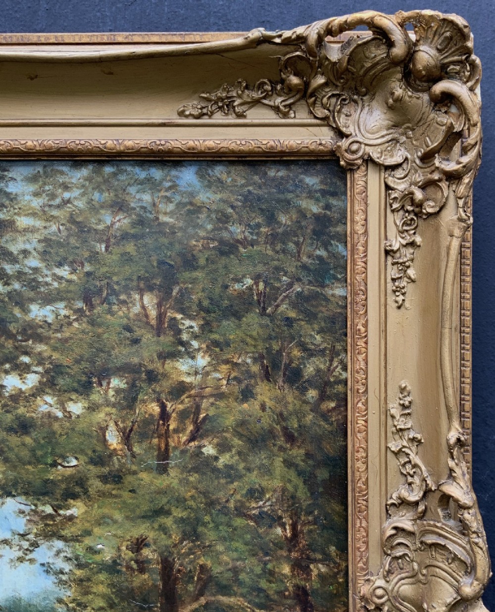 An Edwardian oil painting depicting figures gathered outside a stone church under mature trees, housed within a wide carved gilt frame. View IX
