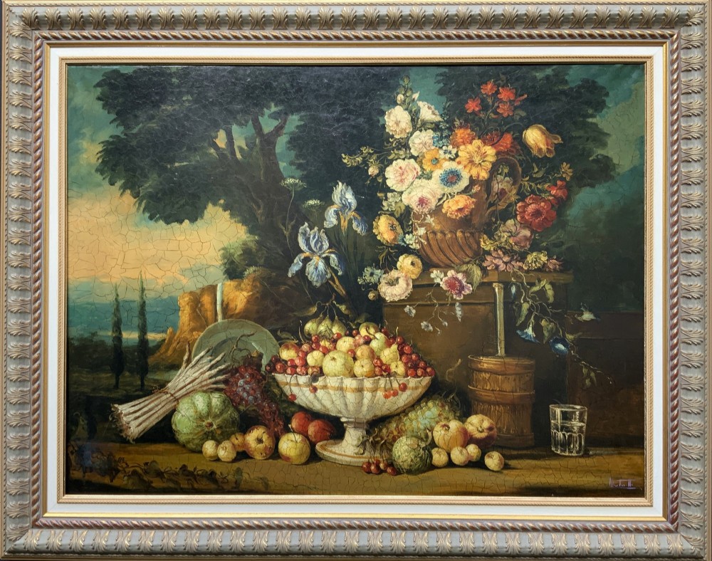 A classical oil painting displaying a bowl of fruit, a urn with flowers, asparagus, and melons set against a dark landscape backdrop within a carved silver-grey frame.