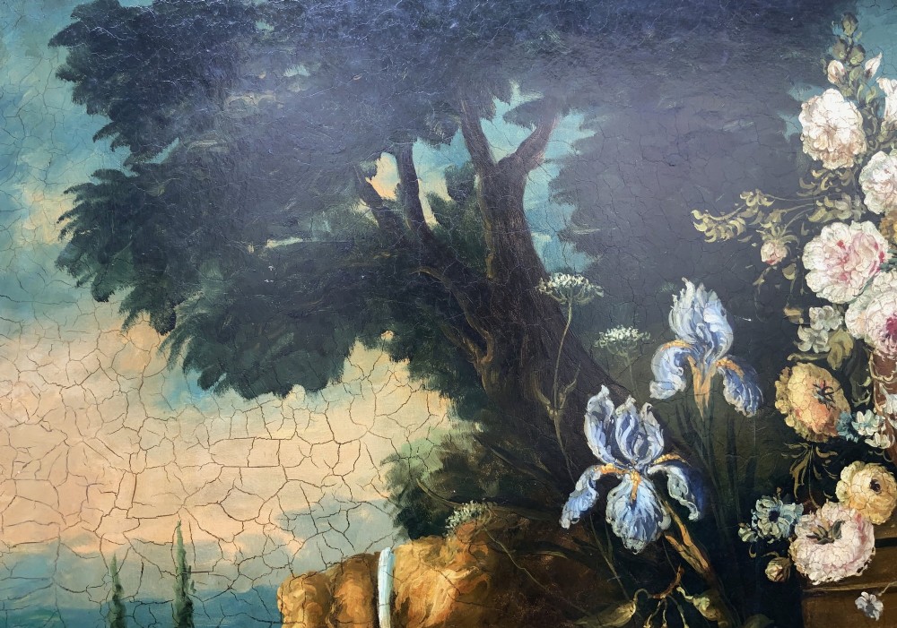 A classical oil painting displaying a bowl of fruit, a urn with flowers, asparagus, and melons set against a dark landscape backdrop within a carved silver-grey frame. View VIII