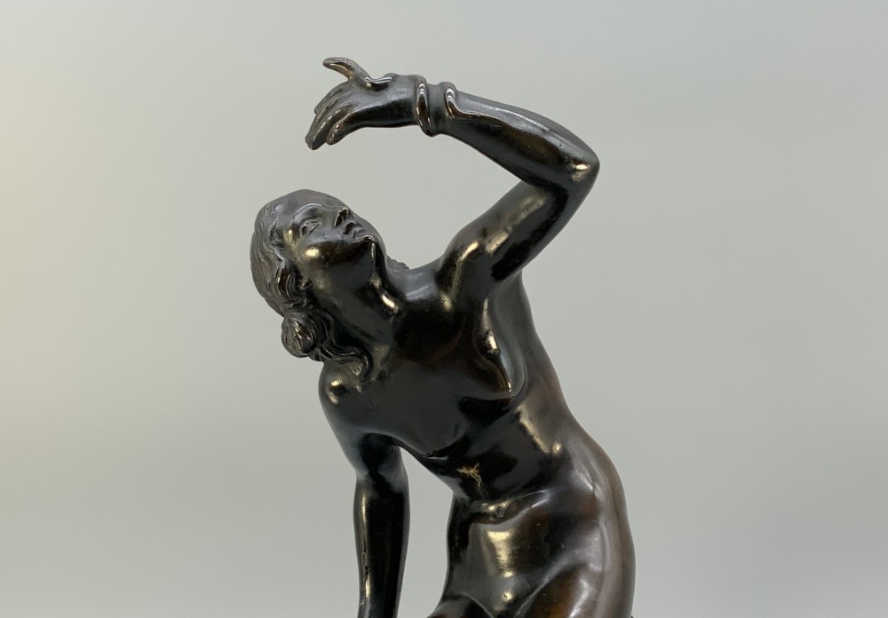 A patinated dark bronze sculpture depicting a classical female figure reaching upward while seated on a rocky outcrop atop a circular marble base. View III