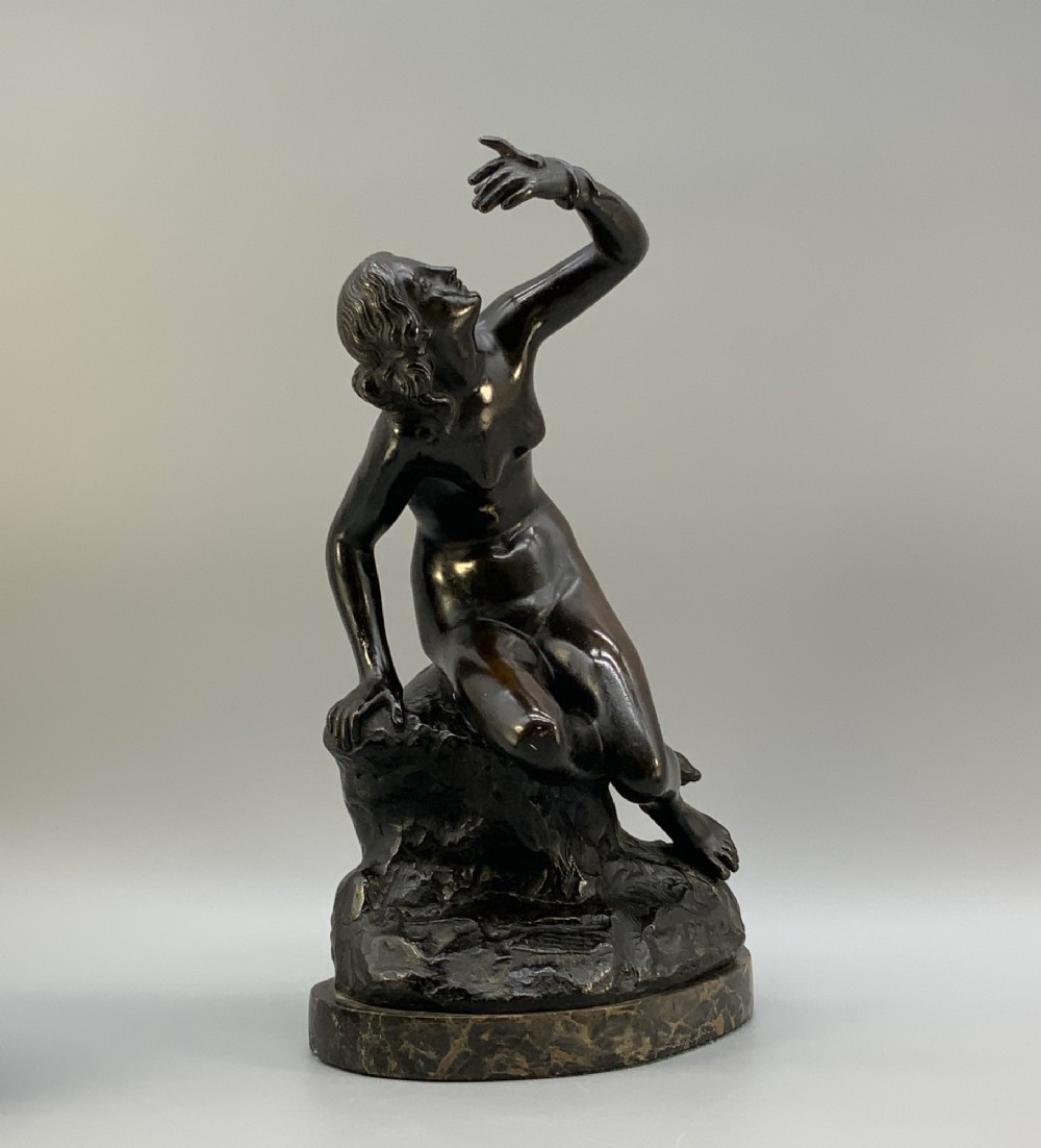 A patinated dark bronze sculpture depicting a classical female figure reaching upward while seated on a rocky outcrop atop a circular marble base. View IV