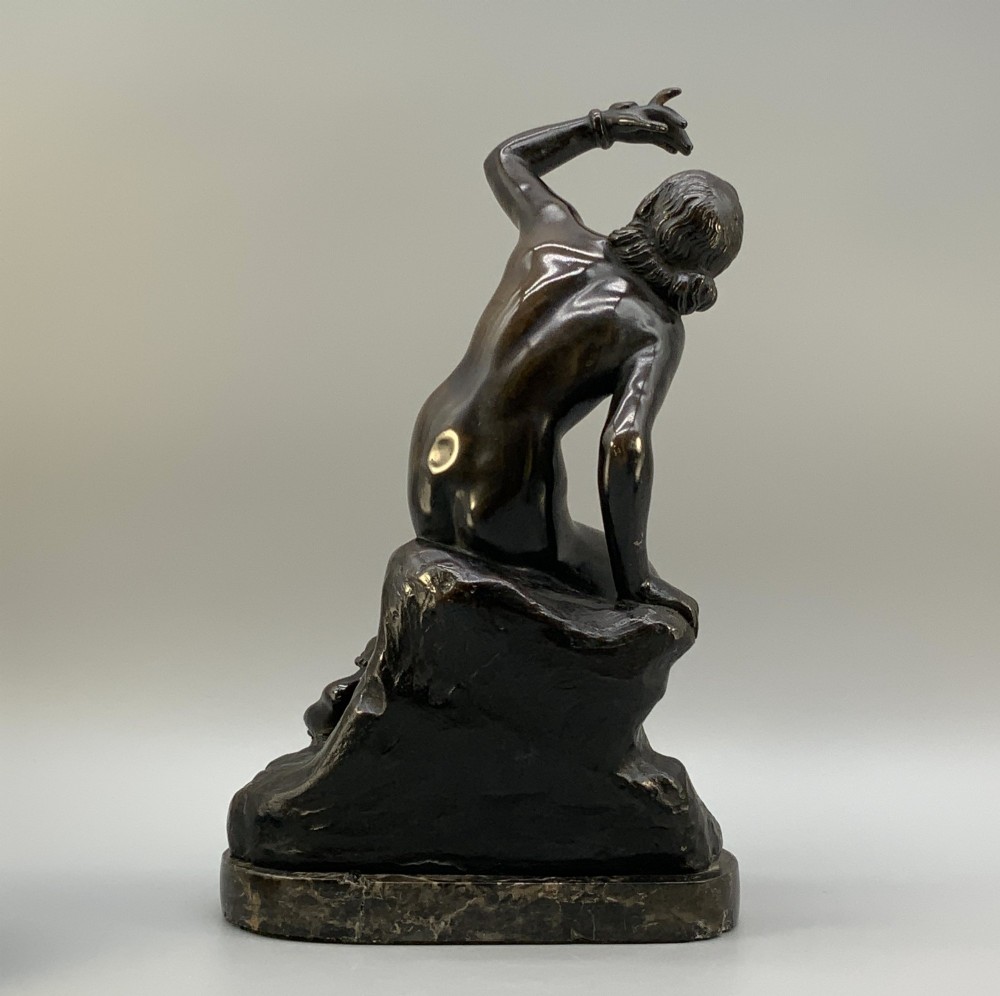 A patinated dark bronze sculpture depicting a classical female figure reaching upward while seated on a rocky outcrop atop a circular marble base. View VI