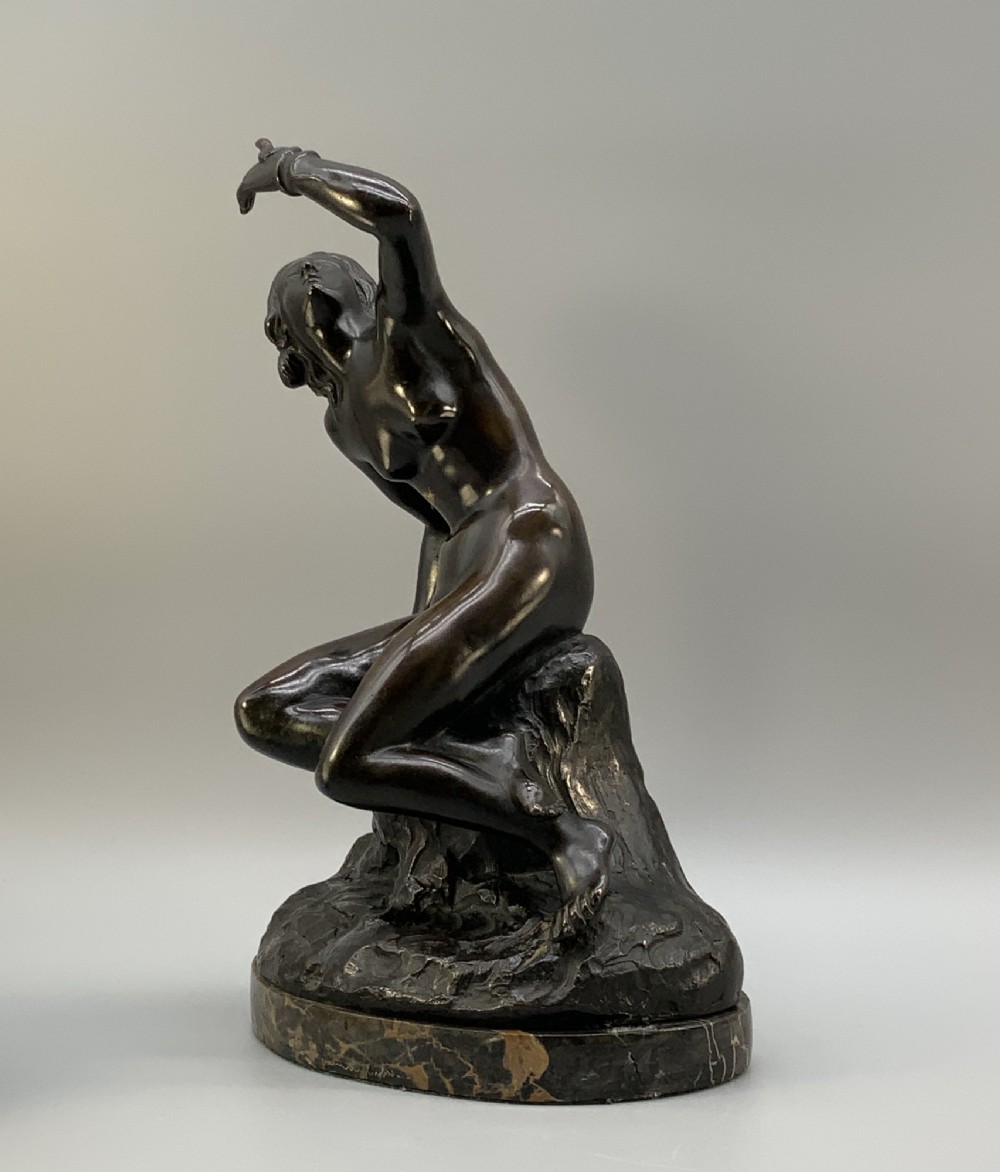 A patinated dark bronze sculpture depicting a classical female figure reaching upward while seated on a rocky outcrop atop a circular marble base. View VIII
