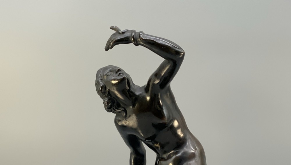 A patinated dark bronze sculpture depicting a classical female figure reaching upward while seated on a rocky outcrop atop a circular marble base. View IX