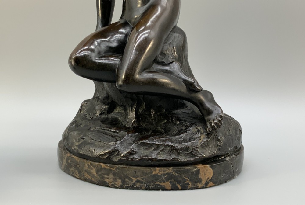 A patinated dark bronze sculpture depicting a classical female figure reaching upward while seated on a rocky outcrop atop a circular marble base. View XI