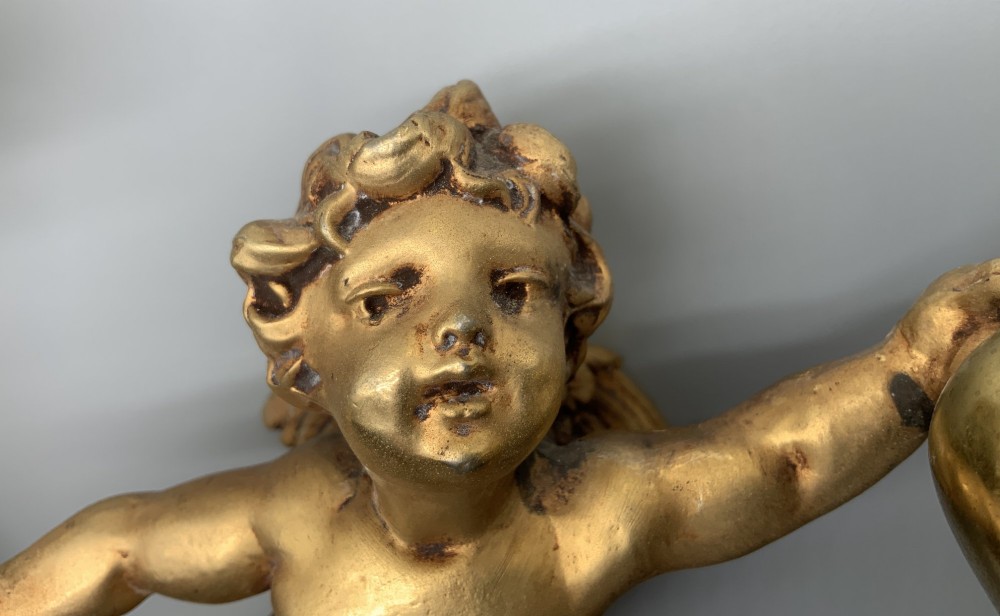A set of three gilt metal wall sconces crafted in the shape of winged cherubs holding bell-shaped light sockets. View IV
