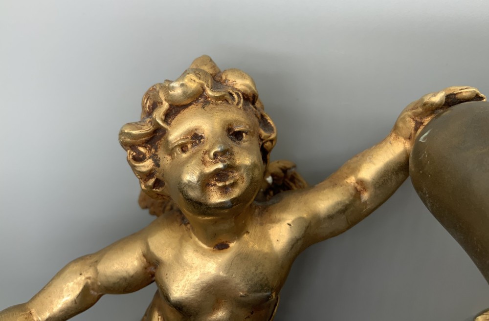 A set of three gilt metal wall sconces crafted in the shape of winged cherubs holding bell-shaped light sockets. View V