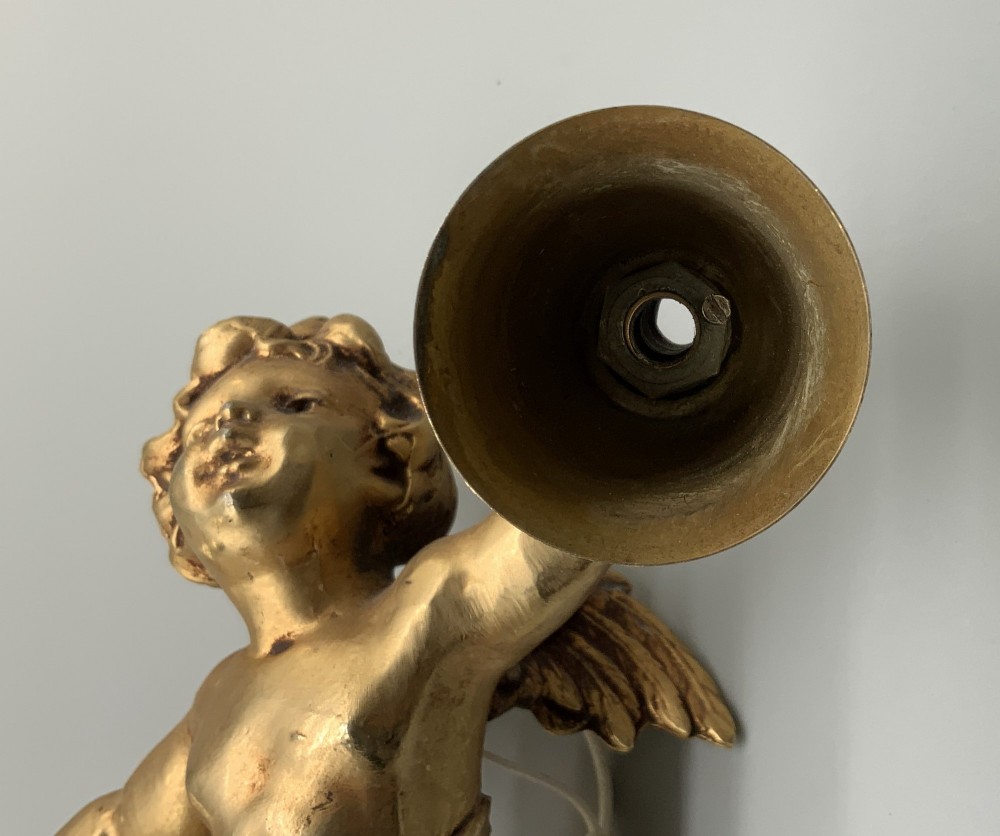 A set of three gilt metal wall sconces crafted in the shape of winged cherubs holding bell-shaped light sockets. View X