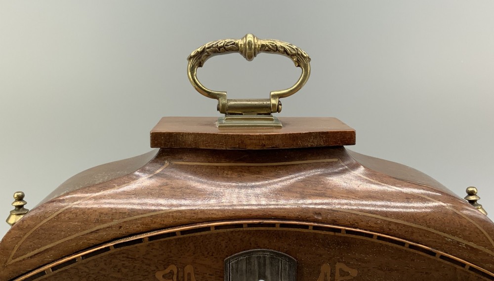 An Edwardian mahogany desk compendium featuring an inlaid floral swag motif, central thermometer, clock dial, barometer dial, and top brass handle. View VI