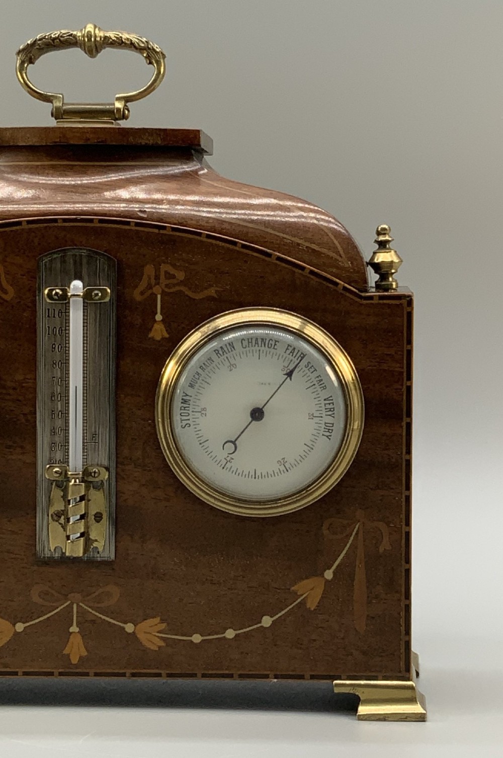 An Edwardian mahogany desk compendium featuring an inlaid floral swag motif, central thermometer, clock dial, barometer dial, and top brass handle. View VII