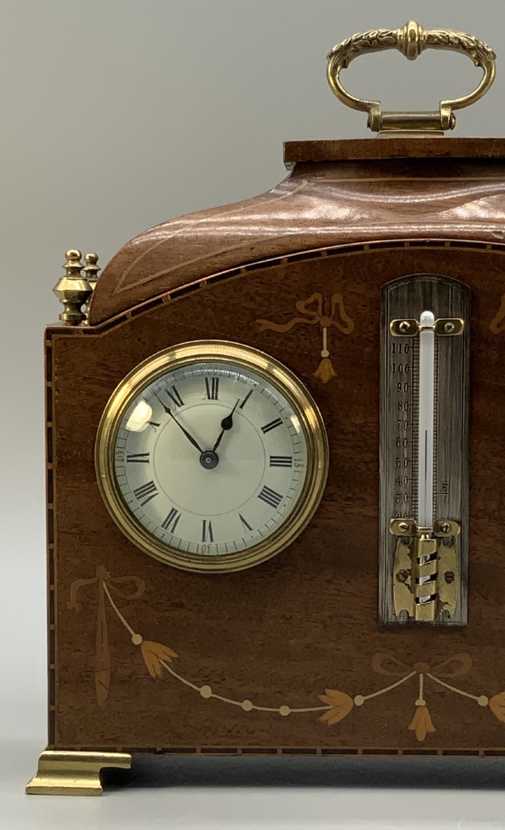 An Edwardian mahogany desk compendium featuring an inlaid floral swag motif, central thermometer, clock dial, barometer dial, and top brass handle. View VIII