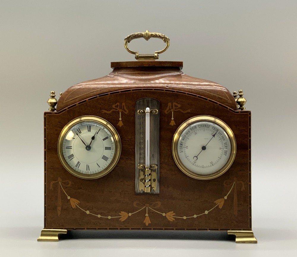 An Edwardian mahogany desk compendium featuring an inlaid floral swag motif, central thermometer, clock dial, barometer dial, and top brass handle. View IX