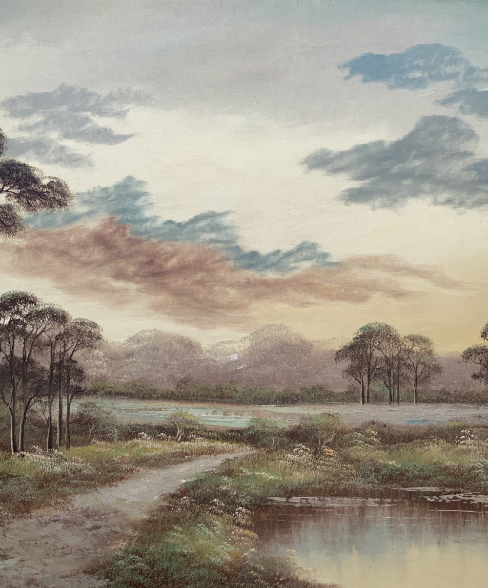 A twentieth-century framed oil painting depicting a countryside path alongside a reflective pond, surrounded by tall trees and distant hills under a clouded sky. View V