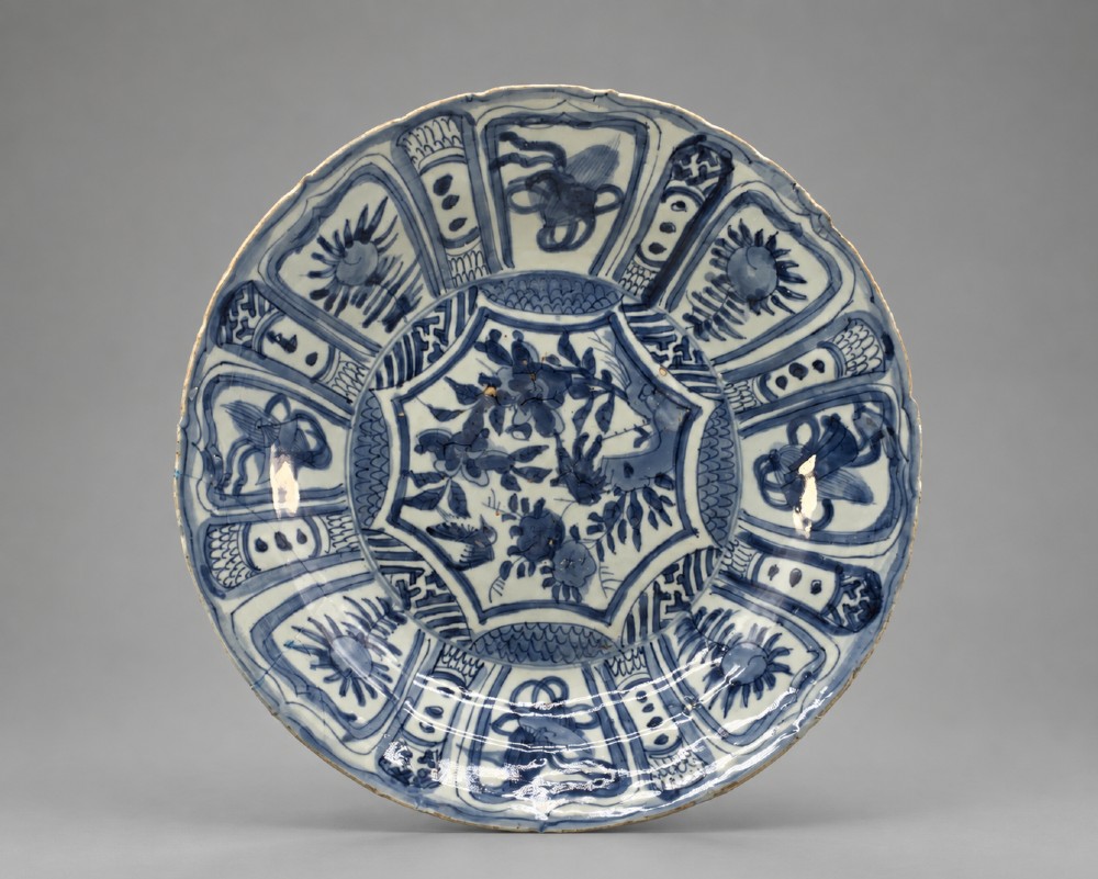 A circular 16th-century Chinese Kraak porcelain charger decorated in cobalt blue underglaze featuring a central floral scene surrounded by a panelled foliate rim.