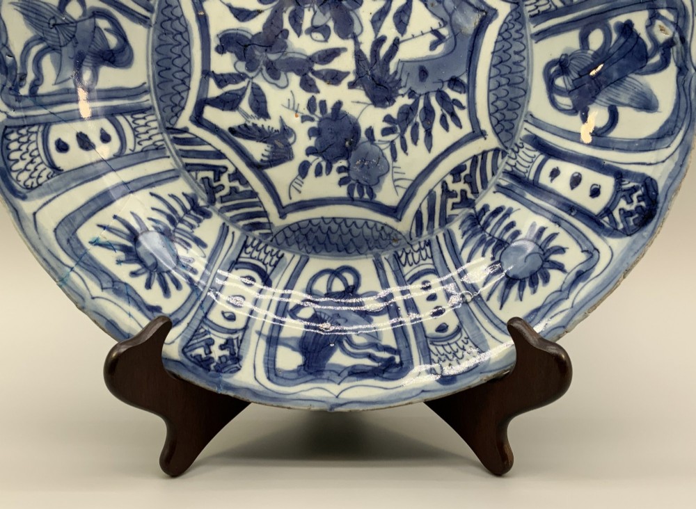 A circular 16th-century Chinese Kraak porcelain charger decorated in cobalt blue underglaze featuring a central floral scene surrounded by a panelled foliate rim. View IV