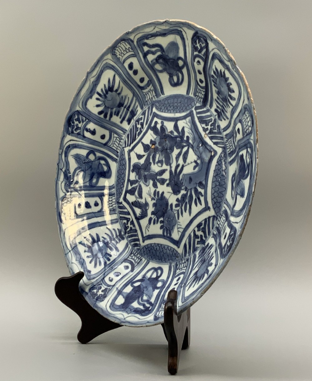 A circular 16th-century Chinese Kraak porcelain charger decorated in cobalt blue underglaze featuring a central floral scene surrounded by a panelled foliate rim. View IX