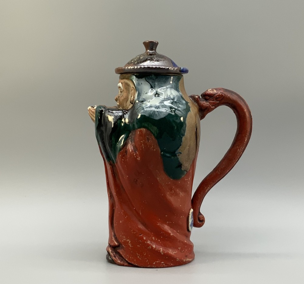 An antique Japanese Sumida Gawa lidded pottery jug sculpted in the form of a robed figure with red attire, green glaze drips, and a matching fitted lid. View III
