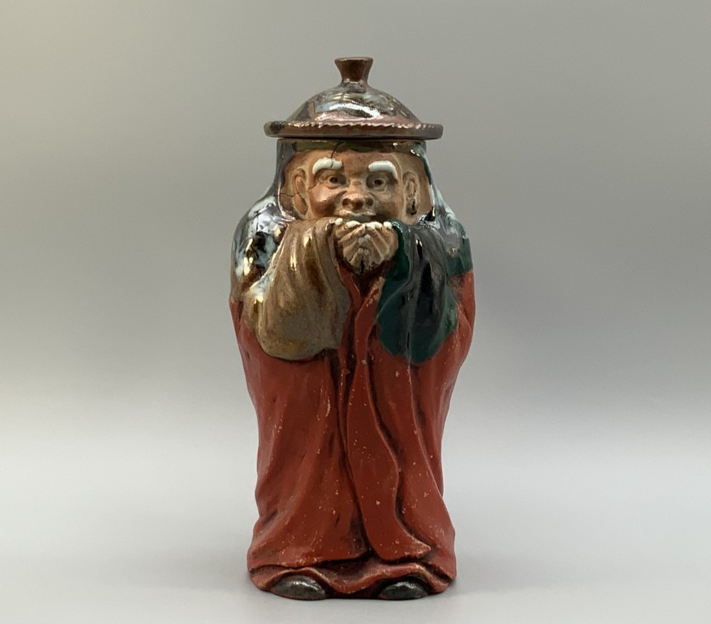An antique Japanese Sumida Gawa lidded pottery jug sculpted in the form of a robed figure with red attire, green glaze drips, and a matching fitted lid. View VI